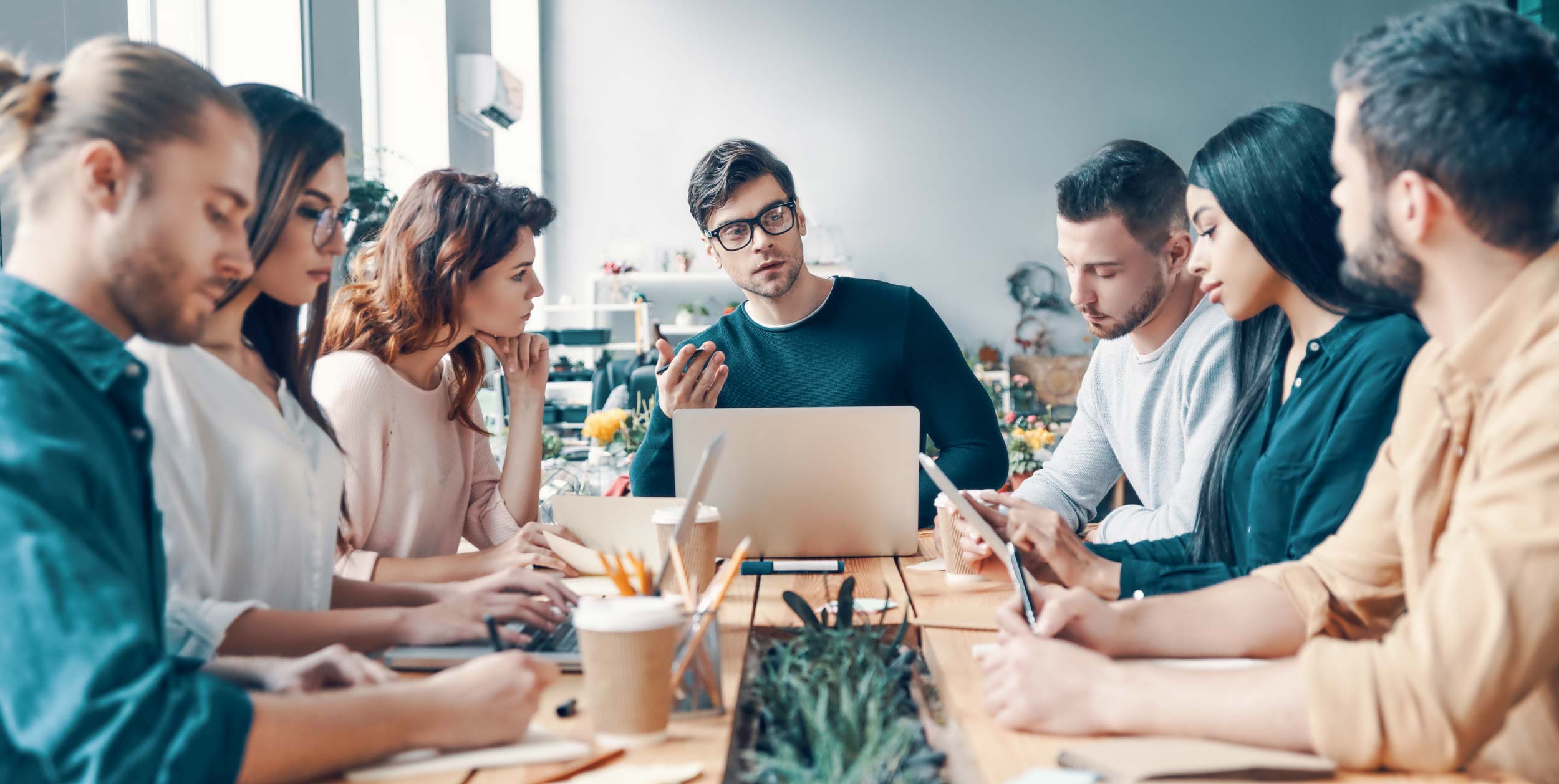 Group of young modern people in smart casual wear discussing something while working in the creative office